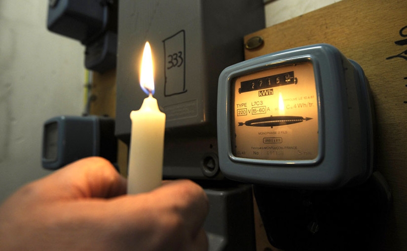 عدد كهرباء أسود اللون لحساب أسعار الكهرباء في المغرب وشخص يحمل بيده شمعة 
